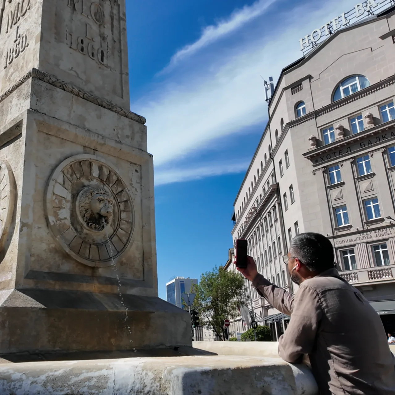 A person using a phone beside an urban monument and clock.